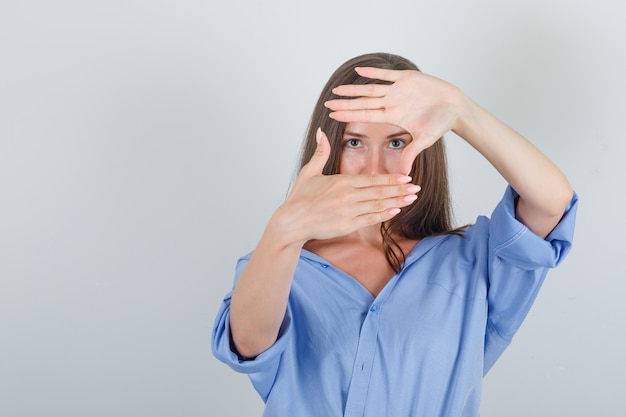 Junge Frau, die Rahmen der Finger im blauen Hemd macht und zuversichtlich schaut