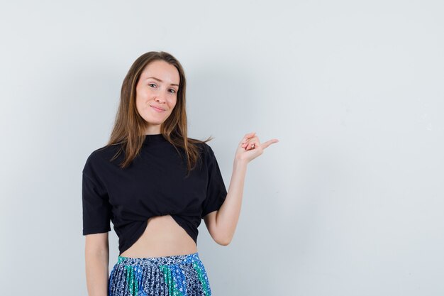 Junge Frau, die rechts mit Zeigefinger im schwarzen T-Shirt und im blauen Rock zeigt und glücklich schaut