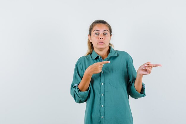 Junge Frau, die rechts mit Zeigefingern in grüner Bluse zeigt und niedlich schaut
