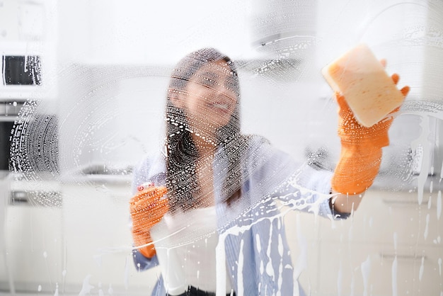 Junge Frau, die schmutziges Fenster mit speziellem Reinigungsmittel putzt