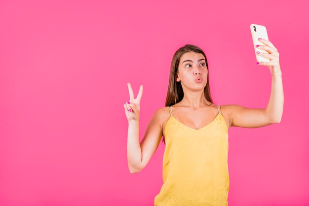 Junge Frau, die selfie auf rosa Hintergrund nimmt