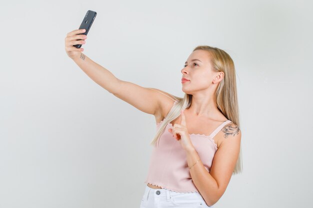 Junge Frau, die selfie mit Finger oben im Unterhemd nimmt