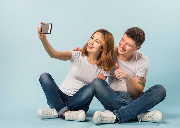 Junge Frau, die selfie mit ihrem Freund zeigt Daumen herauf Zeichen nimmt