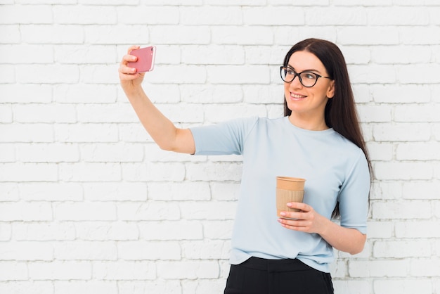 Junge Frau, die selfie mit Kaffeetasse nimmt