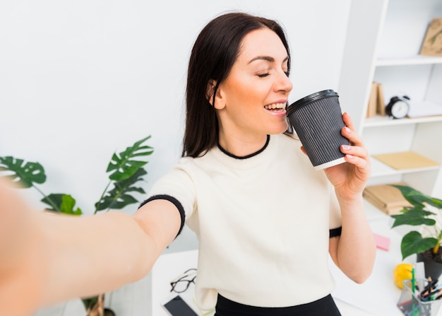 Kostenloses Foto junge frau, die selfie mit kaffeetasse nimmt