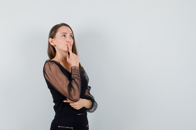 Junge Frau, die sich auf etwas in der schwarzen Bluse konzentriert und nachdenklich aussieht. Vorderansicht. Platz für Text