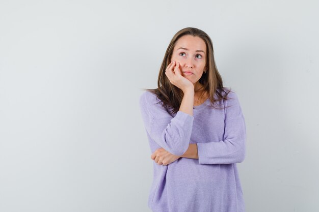 Junge Frau, die sich auf ihre Hand stützt, während sie in der lila Bluse wegschaut und nachdenklich schaut. Vorderansicht.