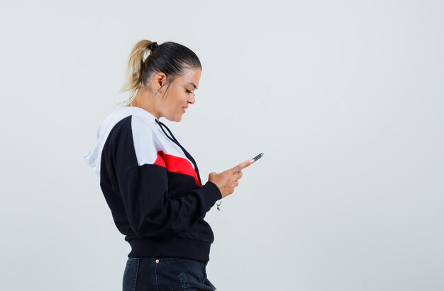 Junge Frau, die sich auf Telefon im bunten Sweatshirt konzentriert und erfreut schaut. .