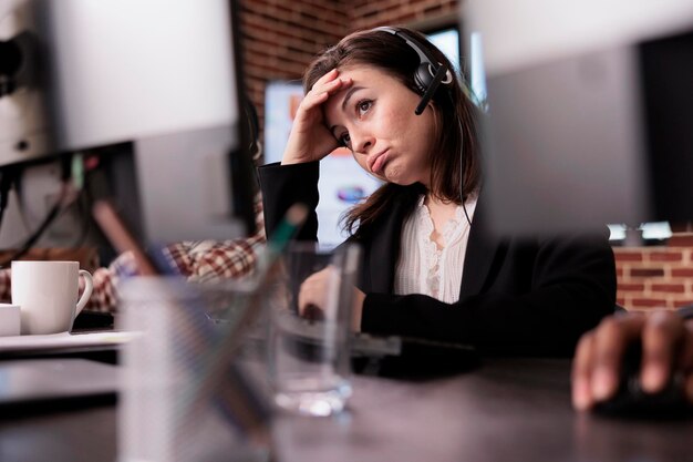 Junge Frau, die sich bei der Kundenbetreuung müde fühlt und am Helpdesk im Telemarketing-Callcenter arbeitet. Weibliche Rezeptionistin mit Helpline-Service, die Kunden bei der Fernkommunikation hilft.