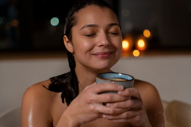 Junge Frau, die sich entspannt und Kaffee trinkt, während sie ein Bad nimmt