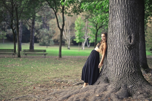 junge Frau, die sich in einem Park an einen Baum lehnt