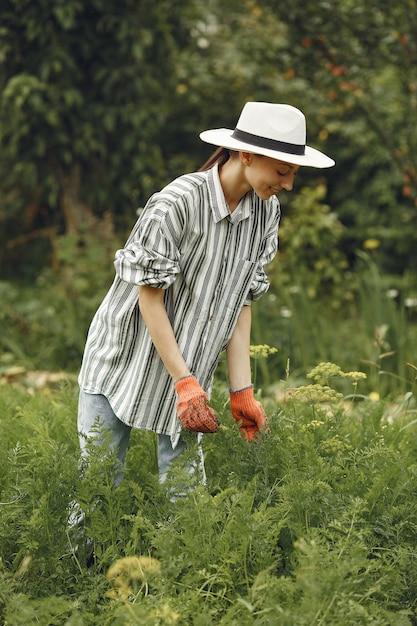 Junge Frau, die sich um Pflanzen kümmert. Brünette mit Hut und Handschuhen.