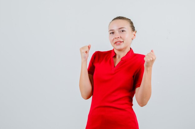 Junge Frau, die Siegergeste im roten T-Shirt zeigt und Glück schaut