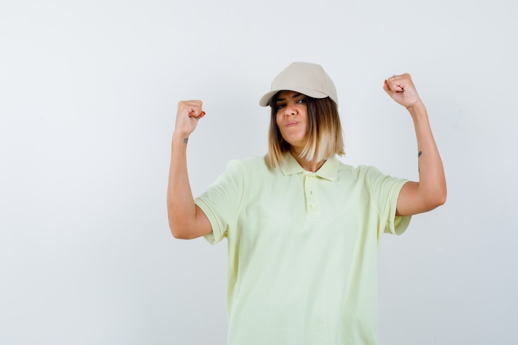 Kostenlose Foto junge frau, die siegergeste im t-shirt, in der kappe und in der glücklichen vorderansicht des glücks zeigt.