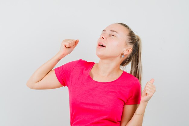 Junge Frau, die Siegergeste im T-Shirt zeigt und friedlich schaut