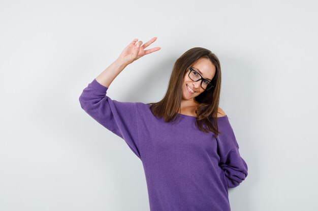 Junge Frau, die Siegeszeichen im violetten Hemd zeigt und fröhlich, Vorderansicht schaut.