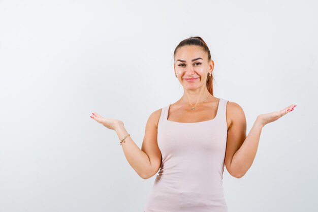 Junge Frau, die Skalengeste im weißen Trägershirt macht und niedlich schaut. Vorderansicht.