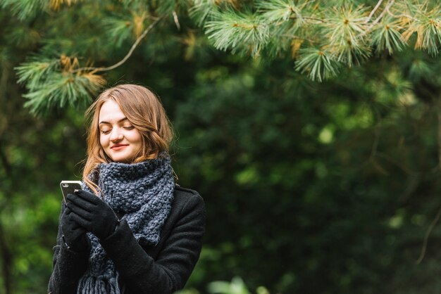 Junge Frau, die Smartphone nahe Koniferenzweigen verwendet