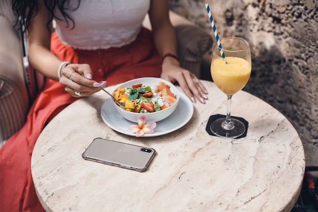 Junge Frau, die Smoothie im Café, glückliches Porträt im Freien isst