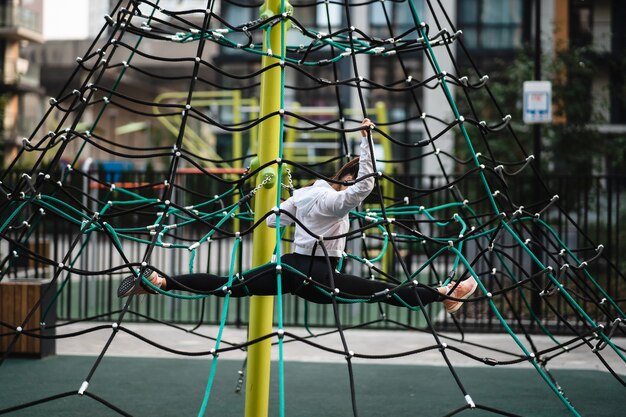 Junge Frau, die Spaß auf der Seilpyramide auf dem Spielplatz hat