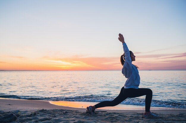 Junge Frau, die Sportübungen am Sonnenaufgangstrand am Morgen tut