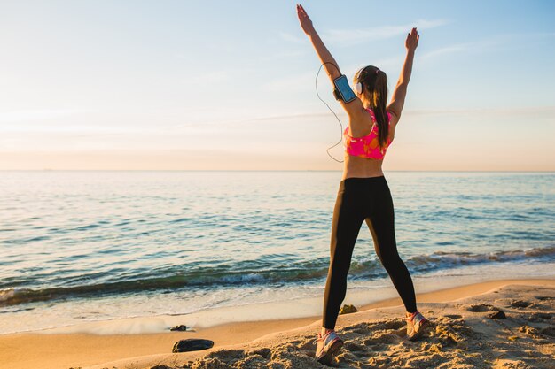 Junge Frau, die Sportübungen am Sonnenaufgangstrand am Morgen tut