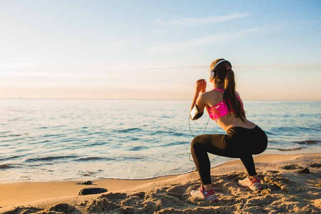Junge Frau, die Sportübungen am Sonnenaufgangstrand am Morgen tut