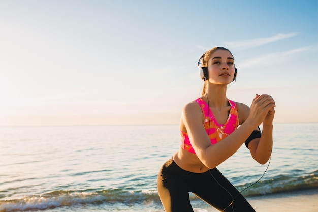 Junge Frau, die Sportübungen am Sonnenaufgangstrand am Morgen tut