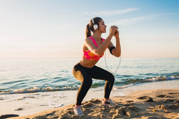 Junge Frau, die Sportübungen am Sonnenaufgangstrand am Morgen tut