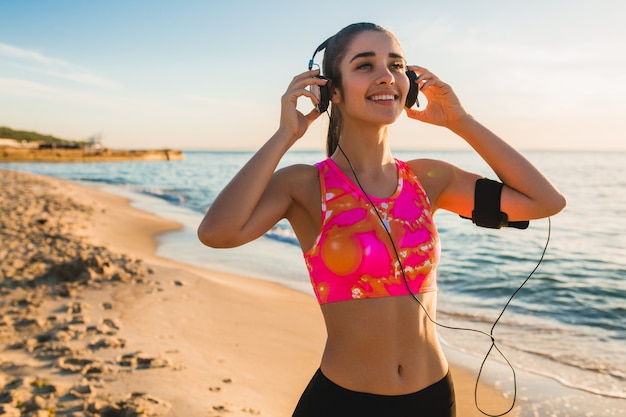 Junge Frau, die Sportübungen am Sonnenaufgangstrand am Morgen tut