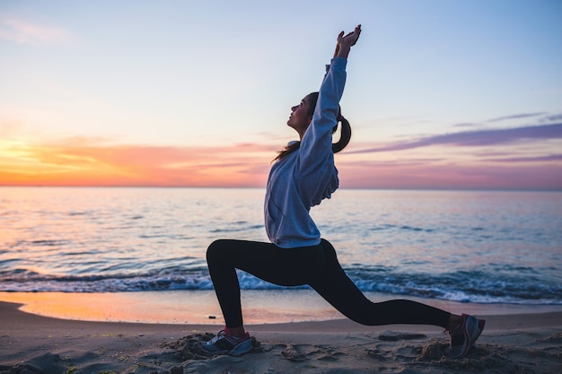 Junge Frau, die Sportübungen am Sonnenaufgangstrand am Morgen tut