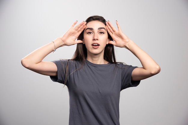 Junge Frau, die steht und ihren Kopf über einem grauen Hintergrund berührt.