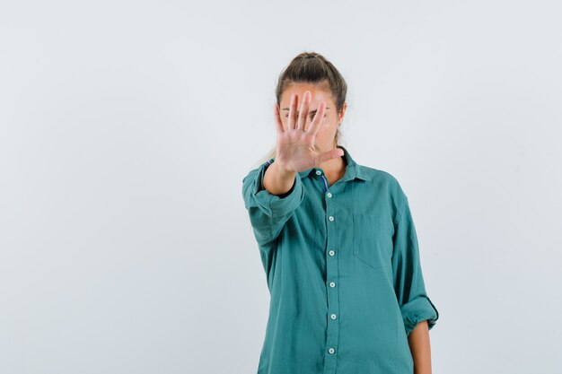 Junge Frau, die Stoppgeste im blauen Hemd zeigt und ernst schaut