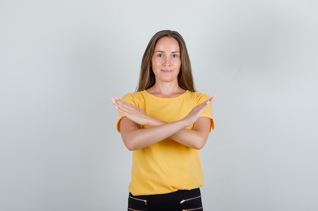 Kostenloses Foto junge frau, die stoppgeste in gelbem t-shirt, hosen zeigt und froh aussieht