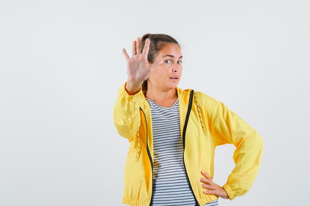 Junge Frau, die Stoppgeste in Jacke, T-Shirt zeigt und selbstbewusst, Vorderansicht schaut.