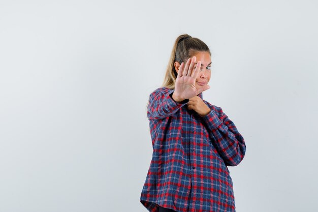 Junge Frau, die Stoppschild im karierten Hemd zeigt und glücklich schaut