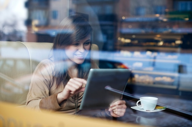 Junge Frau, die Tablette im Kaffeehaus verwendet