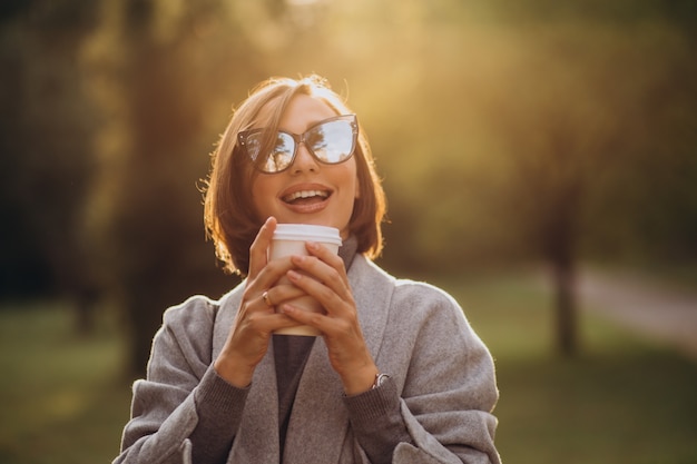 Junge Frau, die Tasse warmen Kaffee im Park hält