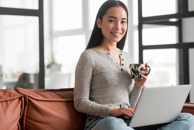 Junge Frau, die Tee trinkt und Laptop verwendet