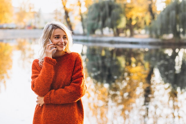 Junge Frau, die Telefon im Park durch den See verwendet