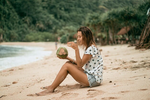 junge Frau, die tropische Kokosnuss am Strand trinkt