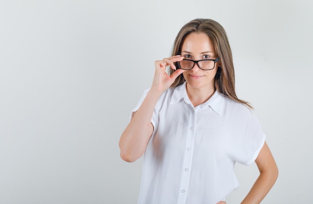 Junge Frau, die über Brille im weißen T-Shirt schaut und fröhlich schaut