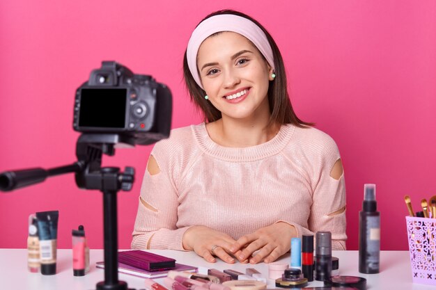 Junge Frau, die über Kamera auf Stativ für ihren vlog über Kosmetik aufzeichnet