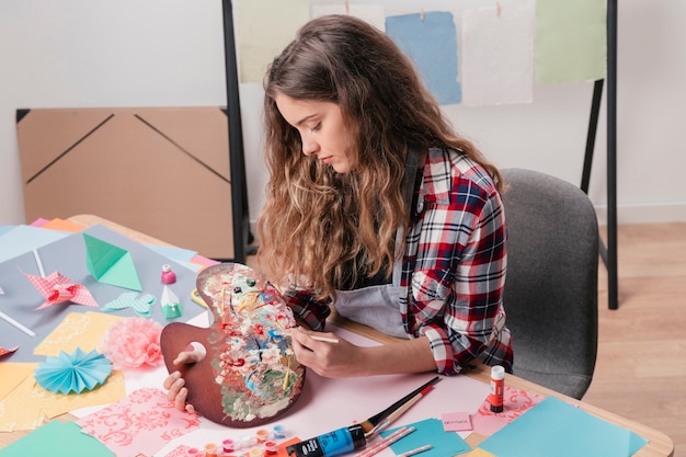 Junge frau, die unordentliche hölzerne aquarellpalette und -pinsel hält