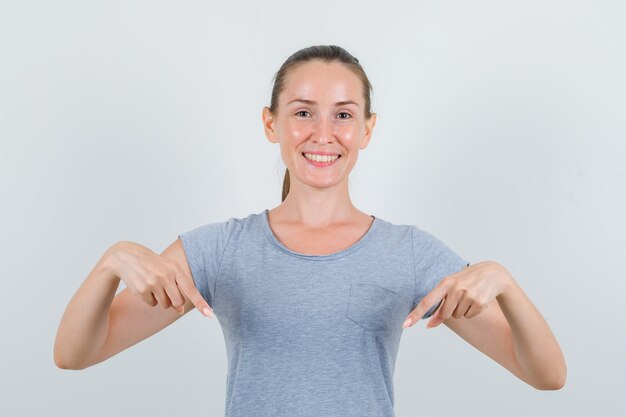 Junge Frau, die unten im grauen T-Shirt zeigt und fröhlich, Vorderansicht schaut.