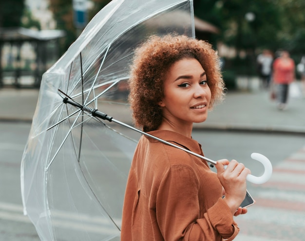 Junge Frau, die unter ihrem Regenschirm steht