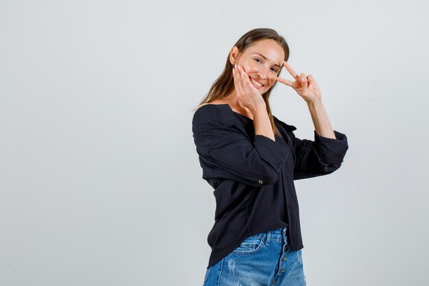 Junge Frau, die V-Zeichen zeigt und im Hemd, Shorts lächelt