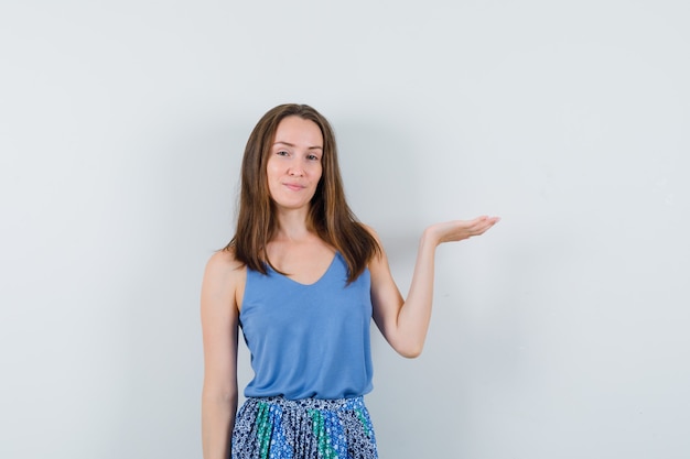 Junge Frau, die vorgibt, etwas im Unterhemd, im Rock zu halten oder zu zeigen und selbstbewusst, Vorderansicht aussehend.