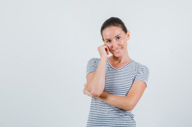 Junge Frau, die Wange auf Hand im T-Shirt lehnt und niedlich schaut. Vorderansicht.