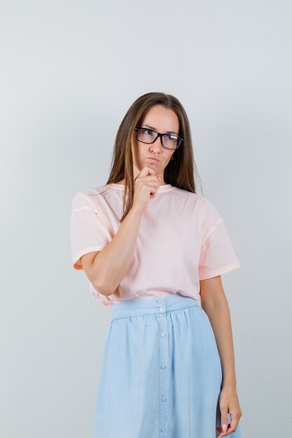 Junge Frau, die weg in T-Shirt, Rock und nachdenklich schaut. Vorderansicht.